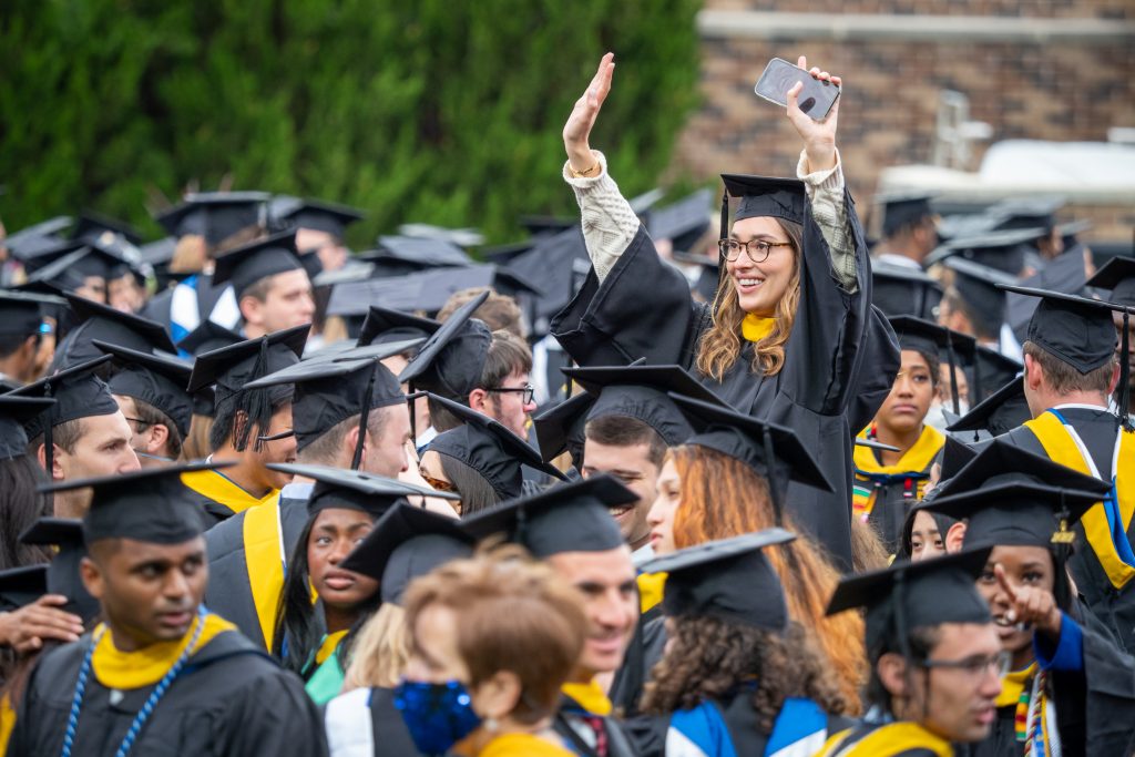 One graduate stands above a sea of mortarboards and waves to the crowd