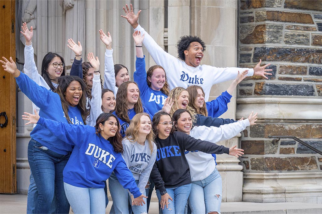 A group of students in Duke gear doing a funny pose in front of the chapel